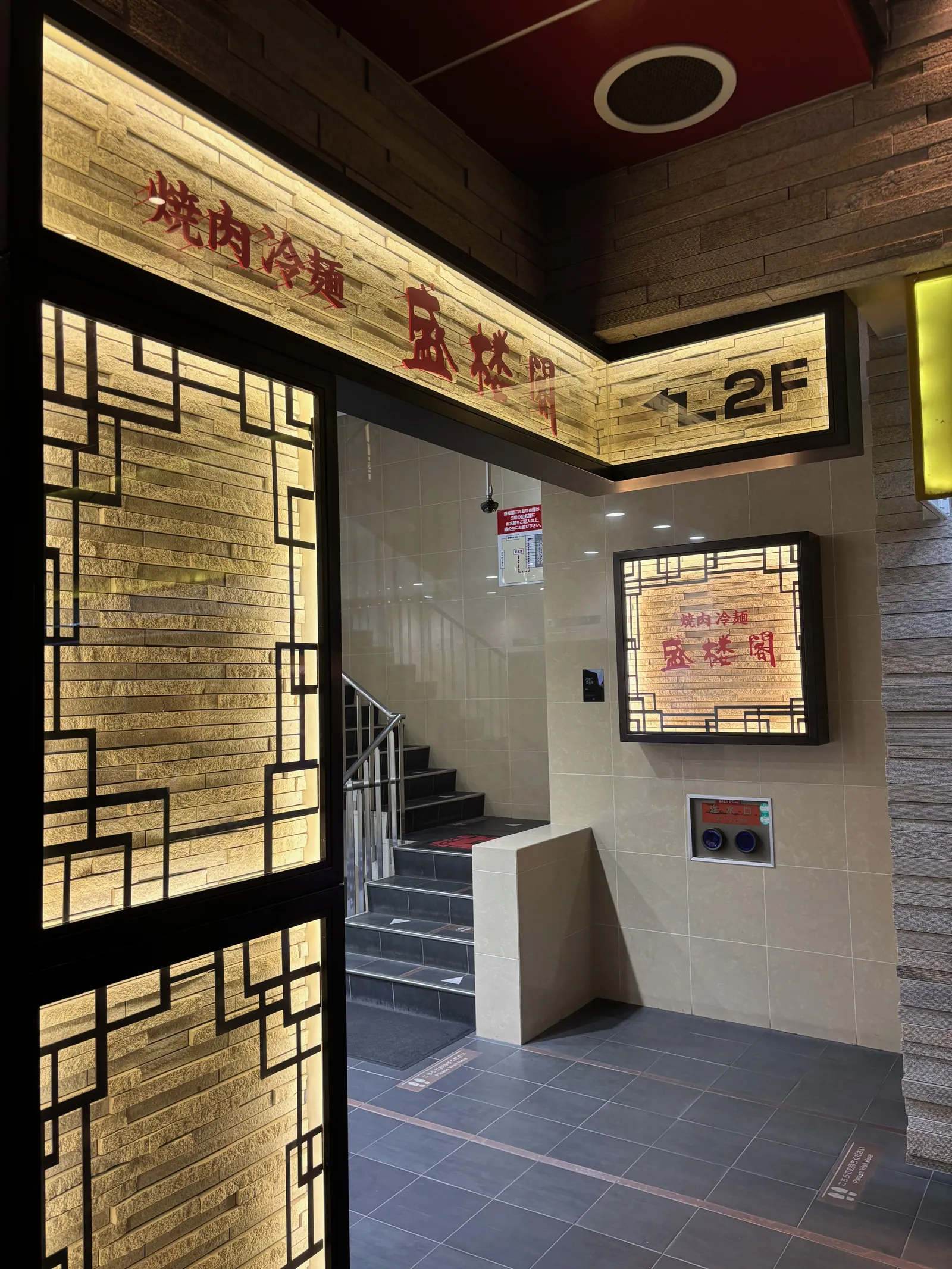 「焼肉冷麺 盛楼閣 →2F」と書かれた案内看板。階段の踊り場に設置されている