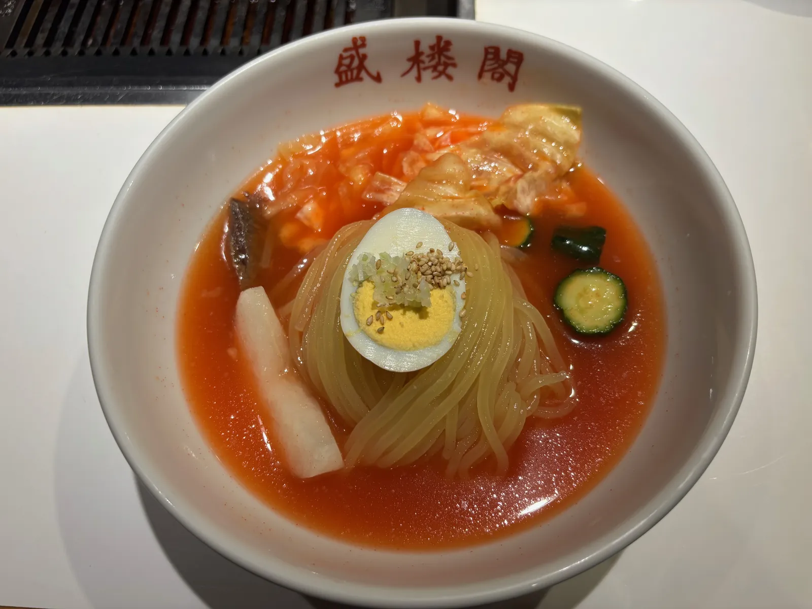 盛楼閣のロゴが入った器に盛られた盛岡冷麺の全体。梨、きゅうり、ゆで卵、キムチ、チャーシューがのっている