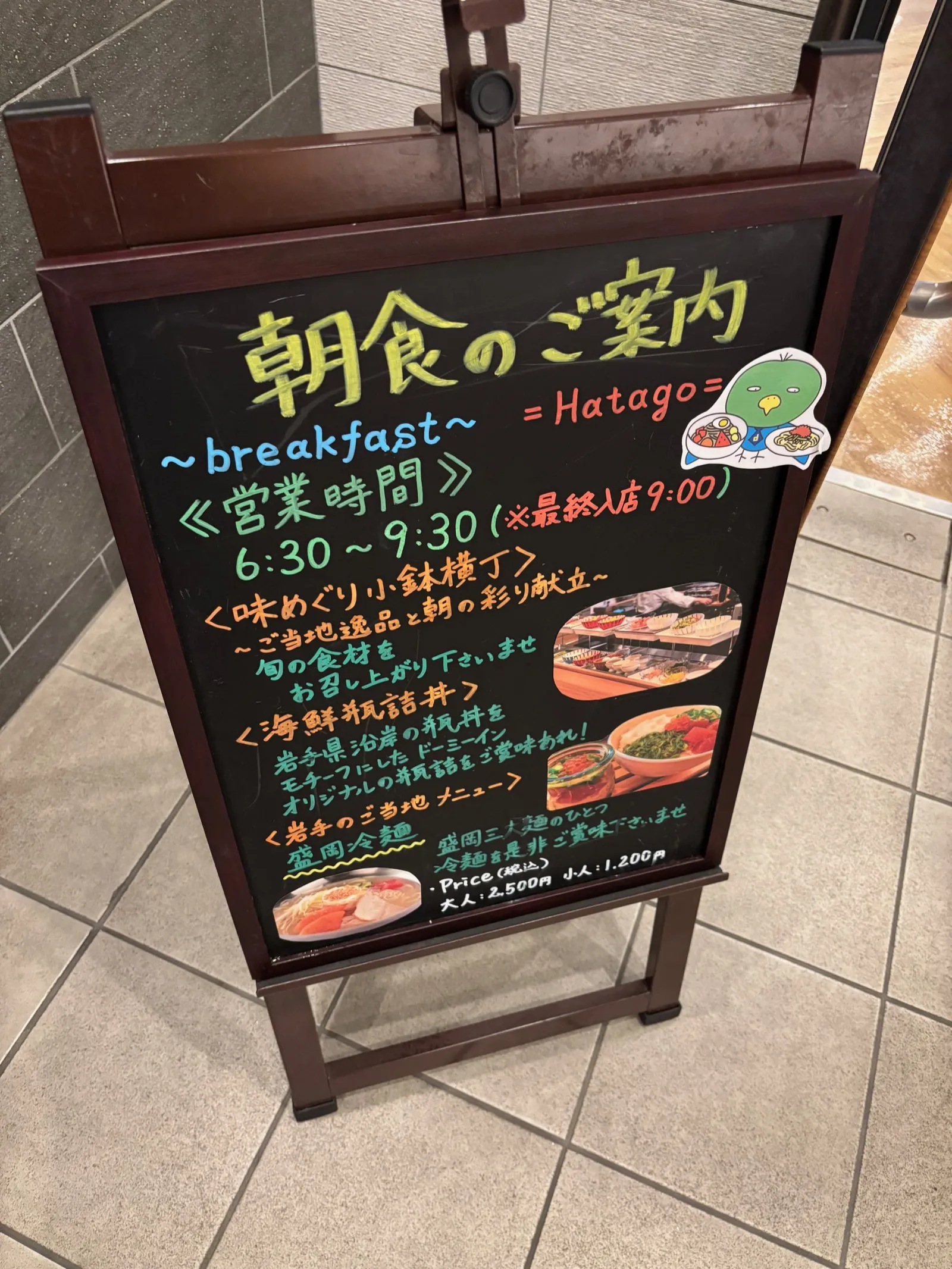 「朝食のご案内」と書かれた黒板看板。営業時間6:30〜9:30（最終入店9:00）、味めぐり小鉢横丁・海鮮瓶詰丼・盛岡冷麺の紹介と価格が書かれている